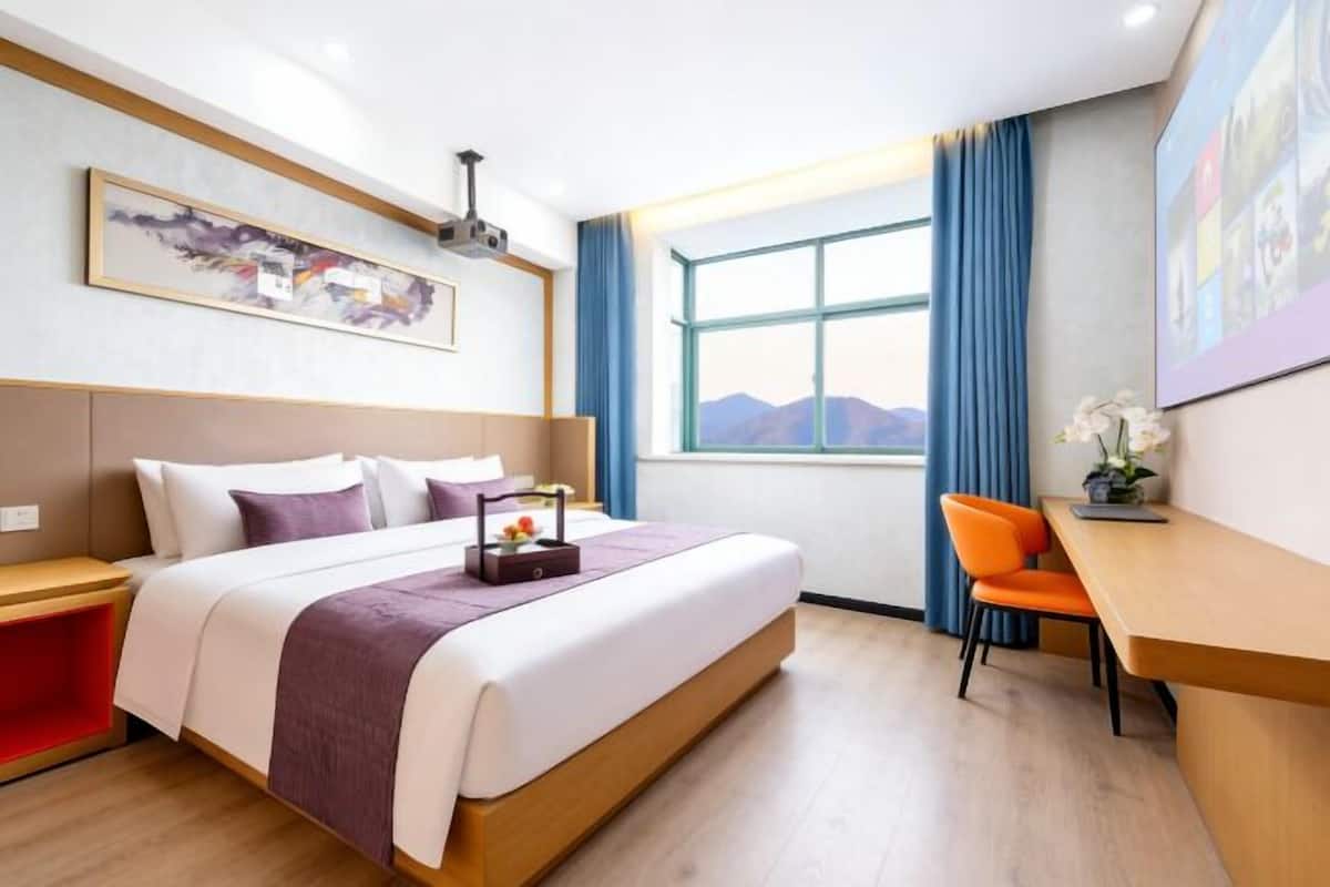 A hotel room with a bed, a desk, a chair, a window with a view, and artwork on the walls.