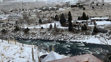 Un paysage montagneux enneigé avec une rivière au premier plan, entouré d’immeubles résidentiels et d’arbres.