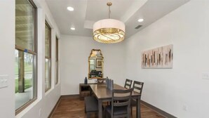 Uma área de refeições com mesa e cadeiras de madeira, uma luminária pendente e um espelho fixado na parede.