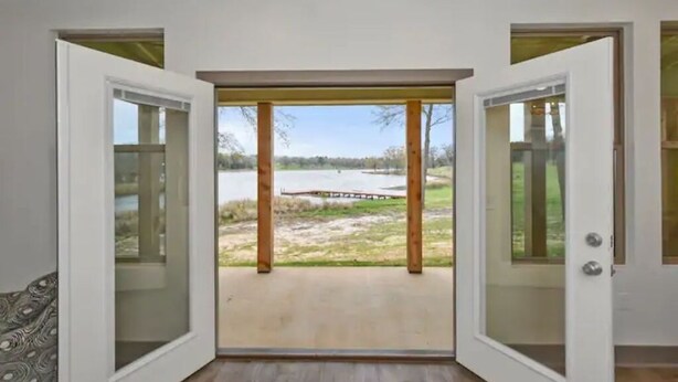 Una habitación con un amplio ventanal corredera que da a un espacio exterior con vista a un lago y una terraza de madera.