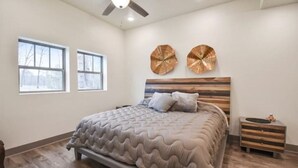 Un dormitorio con una cama grande, dos ventanas, un ventilador de techo y decoración en las paredes.