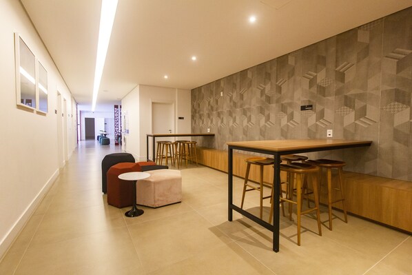 A modern hotel corridor with a bar area featuring stools and a wooden counter.