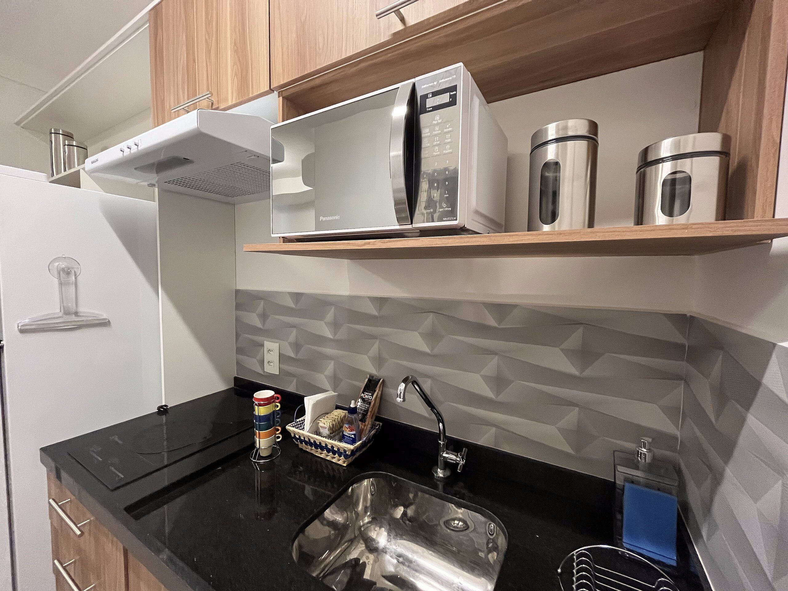 Una cocina moderna con encimera negra, pileta de acero inoxidable y microondas.