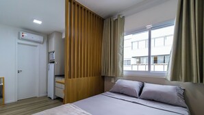 A hotel room with a bed, a desk, an air conditioning unit, and a window with curtains. - Residencial ID Ibirapuera (São Paulo)