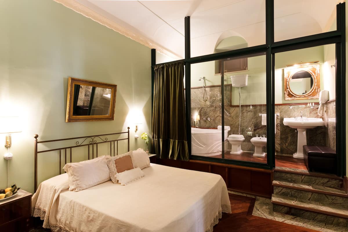 A bedroom with a bed, a nightstand, a mirror, and a view of a bathroom with a marble floor and a sink.