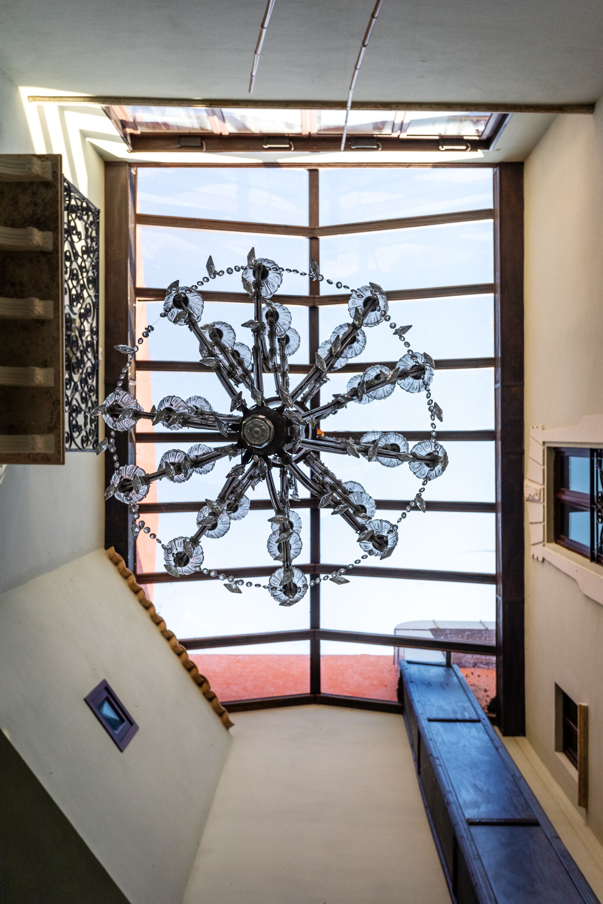 Un intérieur moderne agrémenté d’un grand lustre aux formes géométriques, d’un banc en bois et offrant une vue à travers une grande fenêtre.