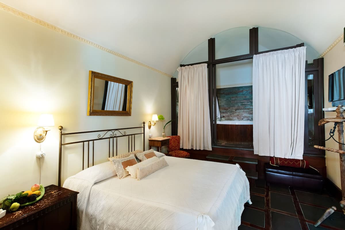 A neatly made bed with pillows, a bedside table with fruits, a lamp, and a mirror on the wall.
