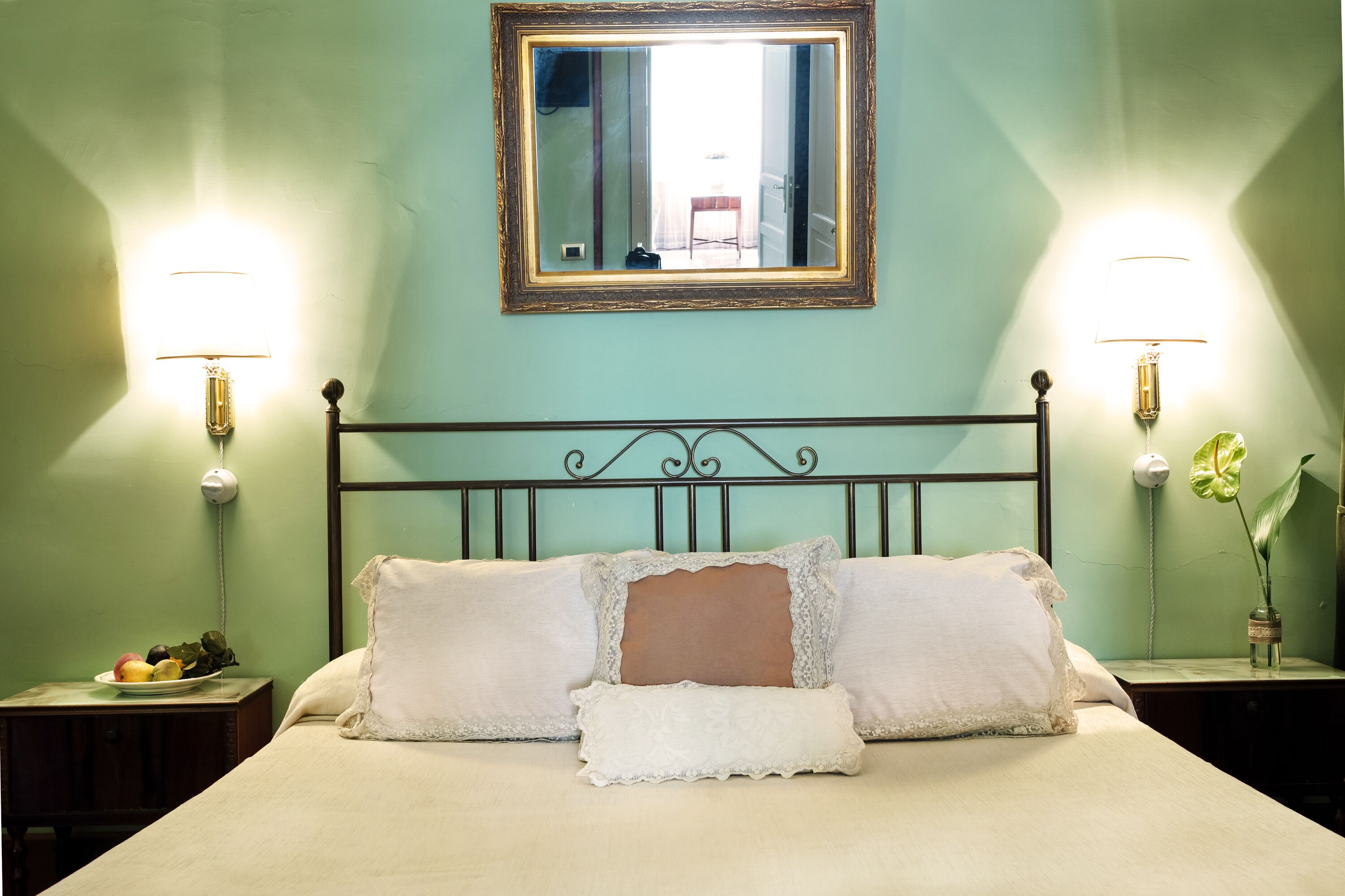Una cama bien hecha con almohadas, una mesita de noche con una lámpara y un jarrón de flores.
