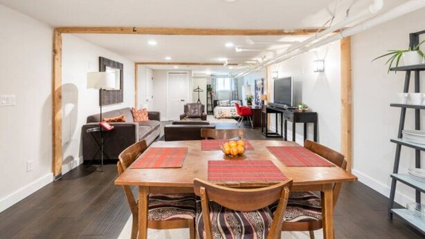 A spacious living area with a wooden dining table, comfortable seating, and a modern kitchen in the background. - A pied-à-terre near bistros, shops, and sports stadium w/ parking and EV charger (Portland)