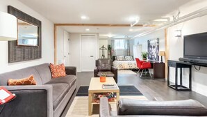 A modern living room with a grey sofa, a leather armchair, a small coffee table, and a TV on a stand. - A pied-à-terre near bistros, shops, and sports stadium w/ parking and EV charger (Portland)