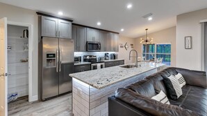 A modern kitchen with stainless steel appliances, a marble island, and a dark leather couch.