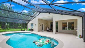 A swimming pool with a turtle floatation device, surrounded by a covered patio with glass walls and a clear view of the outdoors.