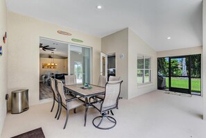 A spacious dining area with a table and chairs, a trash can, and a view of the outdoors through large windows.