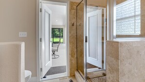 A modern bathroom with a glass shower enclosure, a white toilet, and a door leading to a patio area.