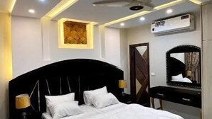 Une chambre à coucher avec une tête de lit noire, du linge de lit blanc, un ventilateur de plafond, des spots encastrés, un tableau, un miroir et un sol en marbre.