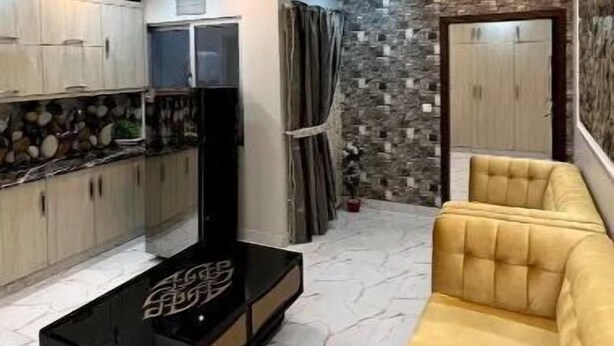 Un salon moderne avec un canapé, une table basse et un téléviseur. Il y a également un coin cuisine avec des placards et un mur en pierre.