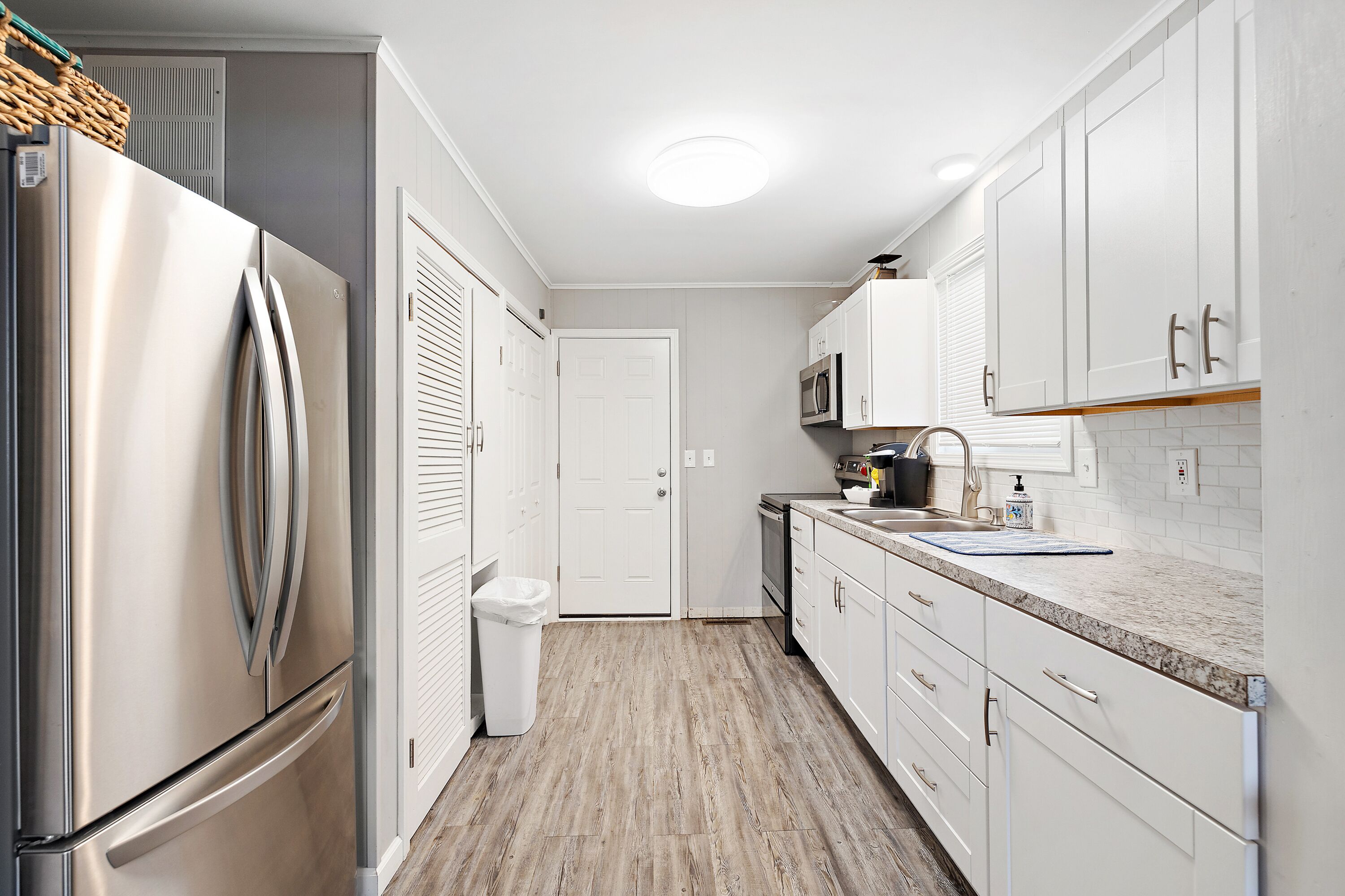 A modern kitchen with white cabinetry, a stainless steel refrigerator, a microwave, and a wooden floor.
