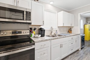 A modern kitchen with white cabinetry, a stainless steel range, a double sink, and a yellow refrigerator. - Cozy Beach House (Lexington)