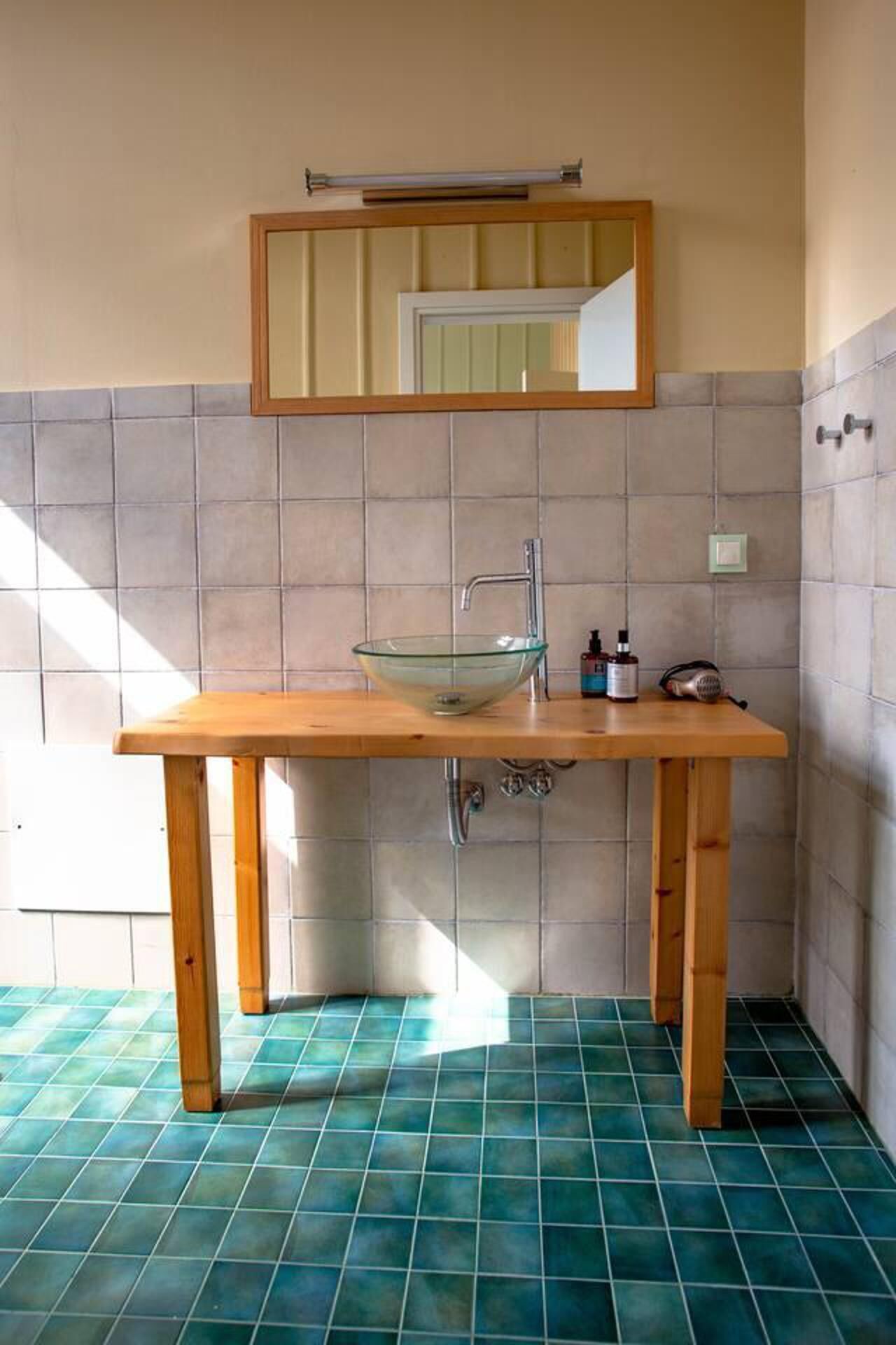 Ein Badezimmer mit Holzwaschtisch, einer Glaskeramik-Spüle, einem Spiegel und gefliesten Wänden sowie Boden.
