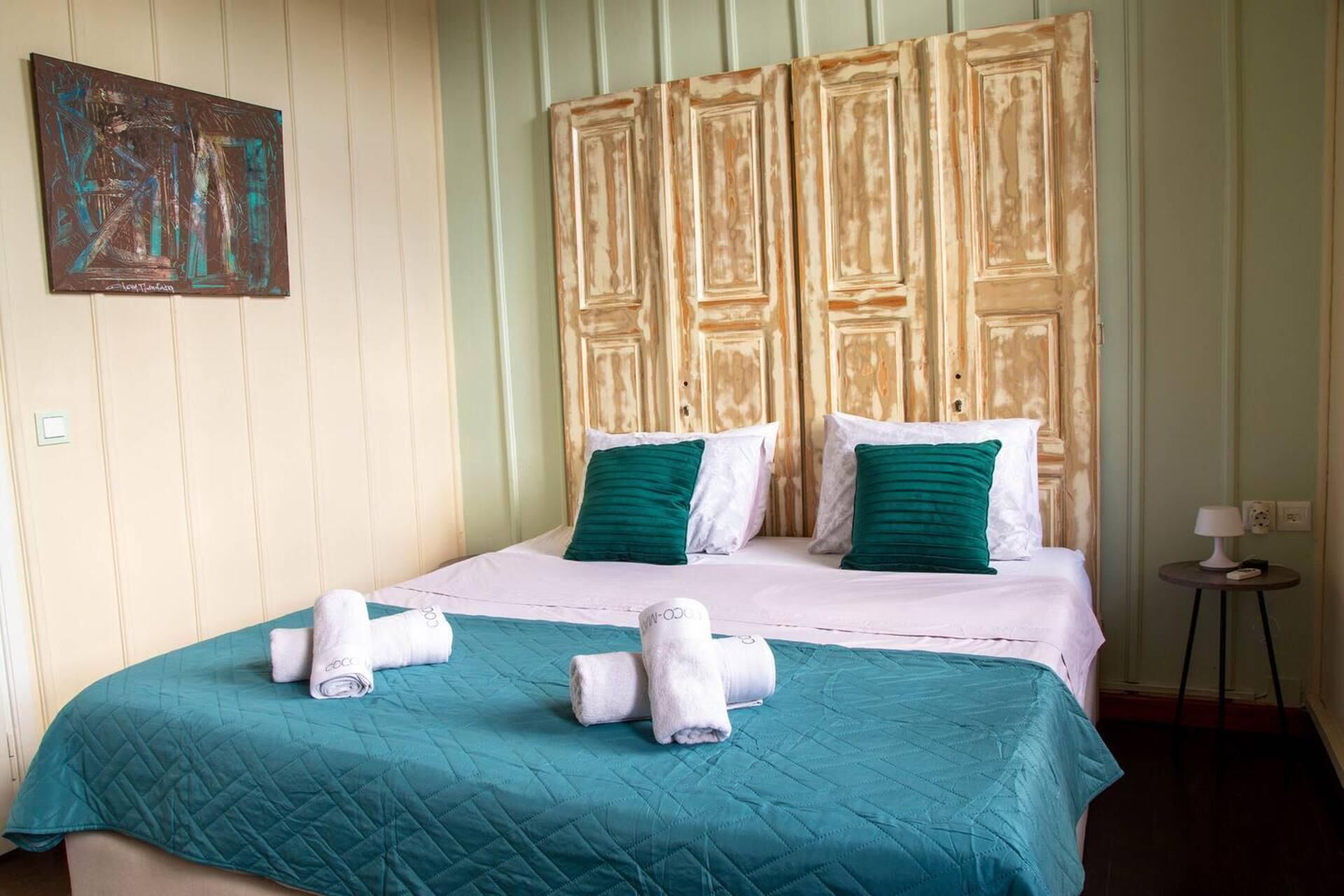 A hotel room with a large bed, teal bedding, white pillows, and a wooden headboard.