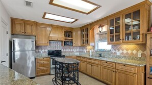 A kitchen with wooden cabinets, a stainless steel refrigerator, a microwave, and a tiled backsplash. - Perfect getaway for all!  Fish and hunt with all the comforts of home! (Port Mansfield)