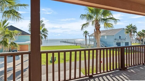 A balcony with a view of a beach, palm trees, and a pier. - Perfect getaway for all!  Fish and hunt with all the comforts of home! (Port Mansfield)