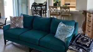 A living room with a teal sofa, a coffee table, and a dining area with a table and chairs. - The Berg Life:  Relax, Fish & Explore the Crystal Co (Marshallberg)