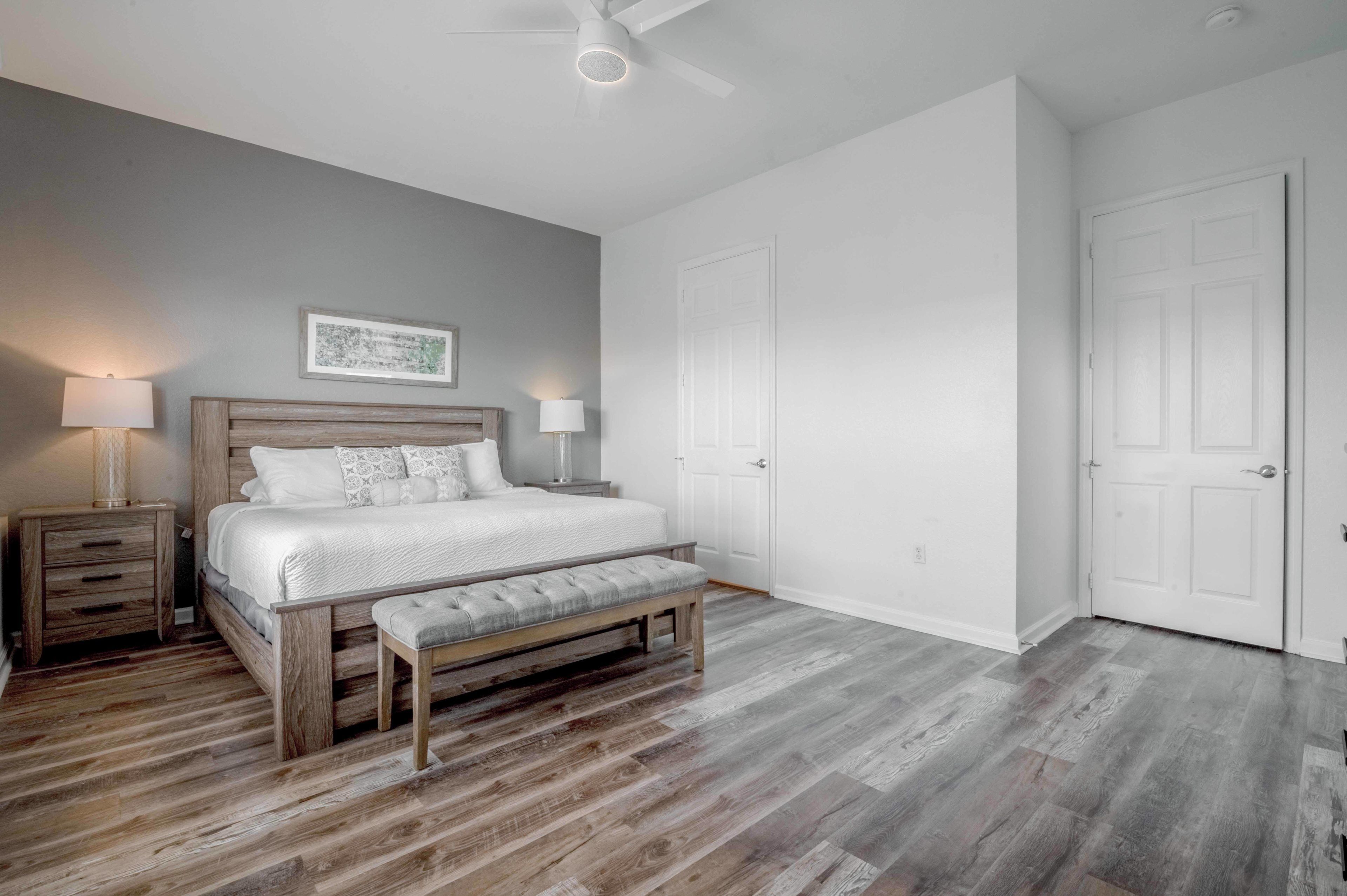 Un dormitorio con una cama de madera, dos mesitas de noche, un banco, un ventilador de techo y una puerta.