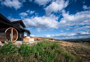 Una casa moderna con un'ampia finestra a botte in legno, immersa in un paesaggio erboso sotto un cielo azzurro terso.