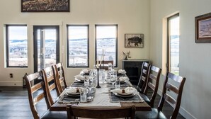 Un comedor con una gran mesa dispuesta para seis personas, ventanas amplias que ofrecen vistas a un paisaje nevado y un cuadro de un búfalo colgado en la pared.