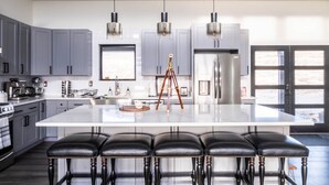 Una cocina moderna con gabinetes grises, una isla grande con taburetes de bar, electrodomésticos de acero inoxidable e iluminación colgante.