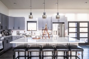 Una cucina moderna con mobili grigi, un'isola grande con sgabelli da bar, elettrodomestici in acciaio inossidabile e luci a sospensione.