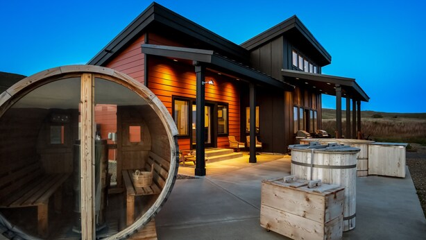 Una casa moderna con fachada de madera, ventanas amplias y un porche con mobiliario exterior.