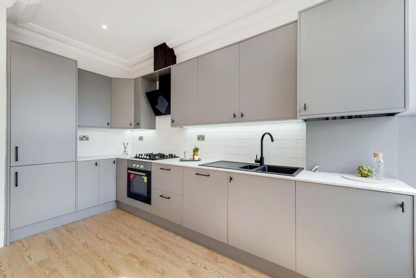 A modern kitchen with grey cabinets, a built-in oven, a gas stove, a sink, and a white countertop.
