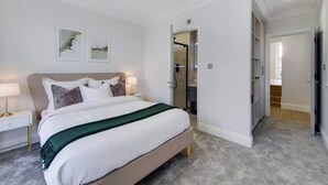 Een slaapkamer met een bed, nachtkastjes, een inloopkast en een badkamer zichtbaar door een geopende deur.