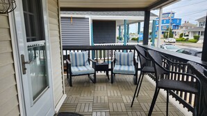 A covered porch with wooden flooring, two striped cushioned chairs, a small table, and a black chair. - Hampton Beach ♡ Ocean Retreat - Steps From The Sand and Strip! (Hampton)