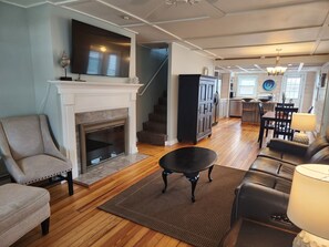 A living room with a fireplace, a staircase, a dining area, and a kitchen.