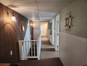 A hallway with a wooden wall, a white railing, a patterned rug, and a wall-mounted decorative piece.