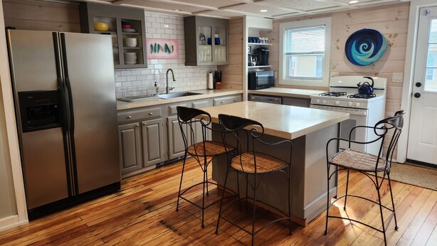 A modern kitchen with a stainless steel refrigerator, a built-in oven, and a large island with bar stools. - Hampton Beach ♡ Ocean Retreat - Steps From The Sand and Strip! (Hampton)