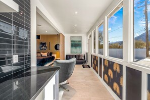 A modern interior with a kitchen area, a seating area with a sofa and armchairs, and a large window offering a view of the outdoors.