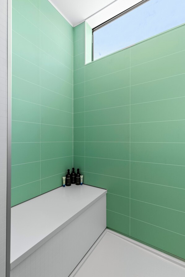 A bathroom with green tiled walls, a white bathtub, and a window.