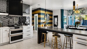 A modern kitchen with a central island, white cabinetry, and a black and gold backsplash.