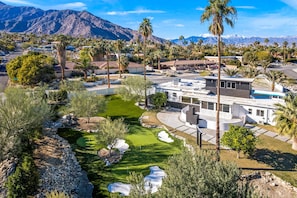 A residential area with a golf course, palm trees, and mountains in the background.