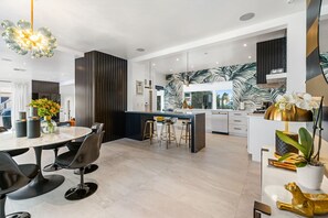 A modern kitchen with a central island, bar stools, and a dining area with a round table and chairs. - Luxury Palm Springs Estate Pool, Spa & Mini-Golf (Palm Springs)