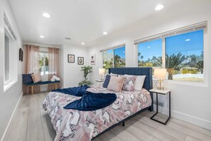 A bedroom with a bed, bedside table, lamp, window, and a bench by the window.