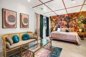 A modern bedroom with a sofa, a glass coffee table, a bed with a floral mural, and a nightstand with a lamp.