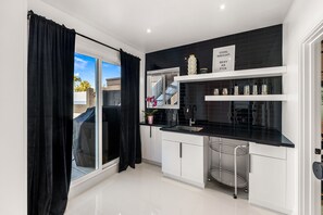 A modern kitchen with black countertops, white cabinets, a black tiled backsplash, and a window with black curtains.