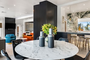 A modern kitchen with a marble island, bar stools, and a large potted plant.