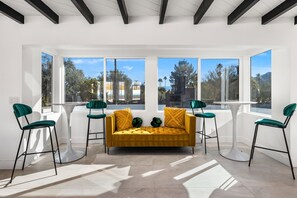 A modern living room with a mustard yellow sofa, green chairs, and large windows offering a view of trees and mountains. - Luxury Palm Springs Estate Pool, Spa & Mini-Golf (Palm Springs)
