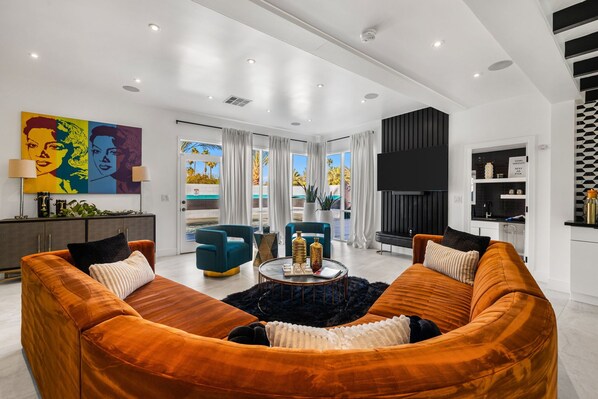 A modern living room with a large orange sofa set, a coffee table, and a colorful artwork on the wall.